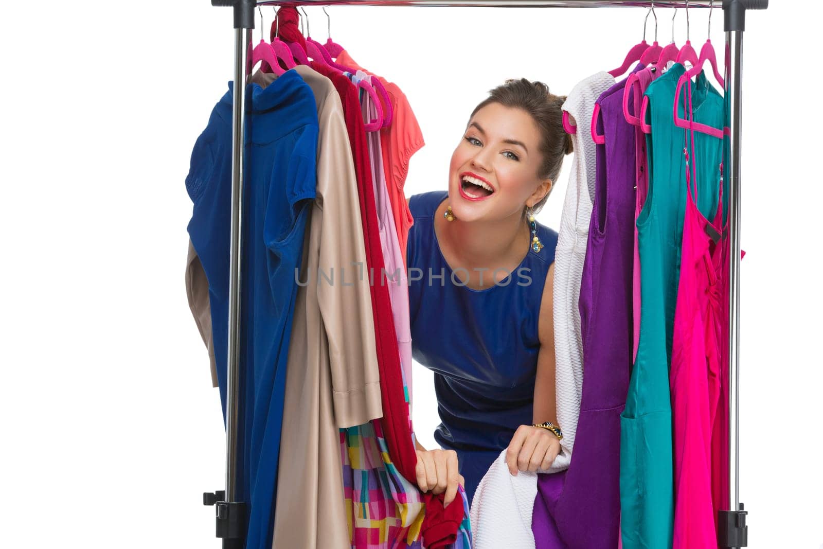 Beautiful happy young woman lookinh through hanger with many dresses. Isolated over white background. Copy space.