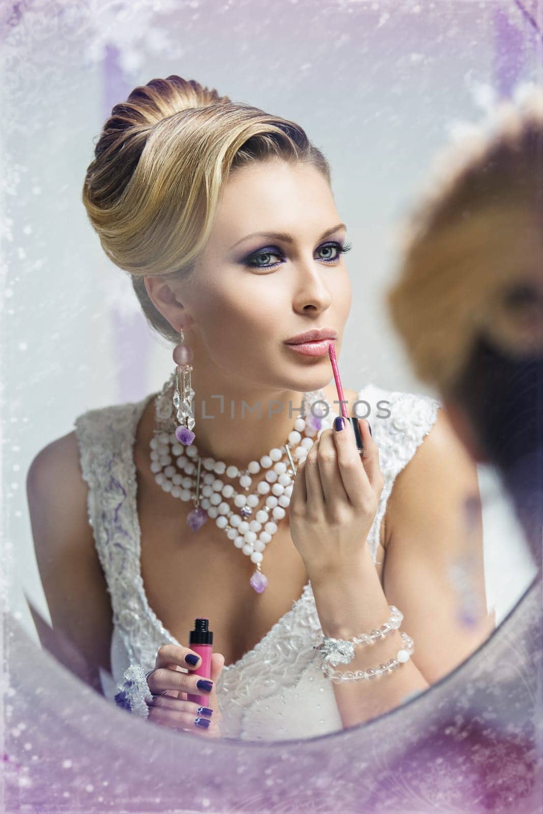 Beautiful young bride looking into mirror and putting on pink lipstick