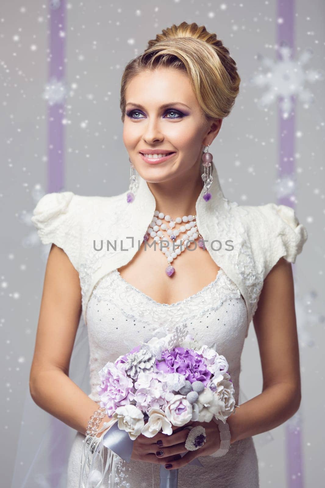 Portrait of beautiful young woman in long warm gown for winter wedding with purple flower bouquet. Over snowy background