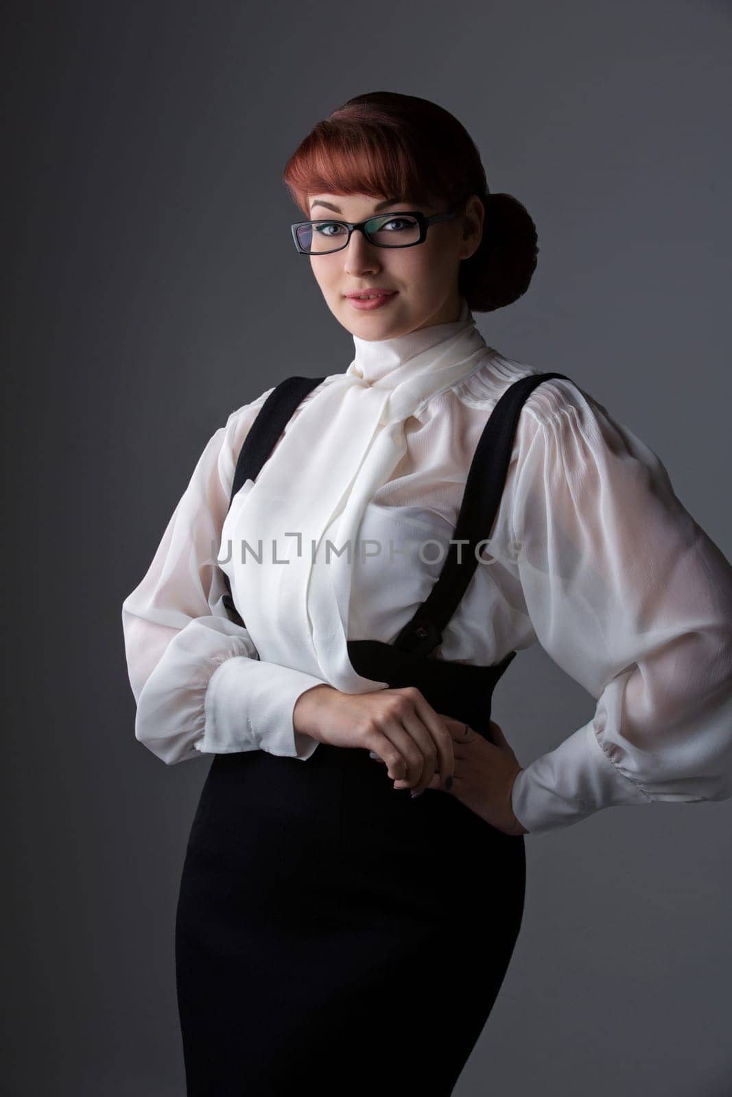 Beautiful young woman in fashionable glasses wearing blouse and skirt. Over grey background. Copy space. Vertical.