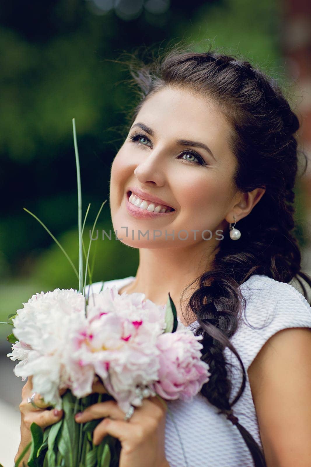 Closeup portrait of beautiful smiling girl with braid holding bouquet of pionies. Outdoor shot.
