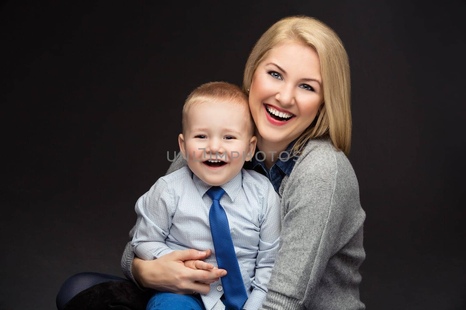 Portrait of beautiful young woman hugging her handsome toddler son. Happy people. Studio shot over dark background.
