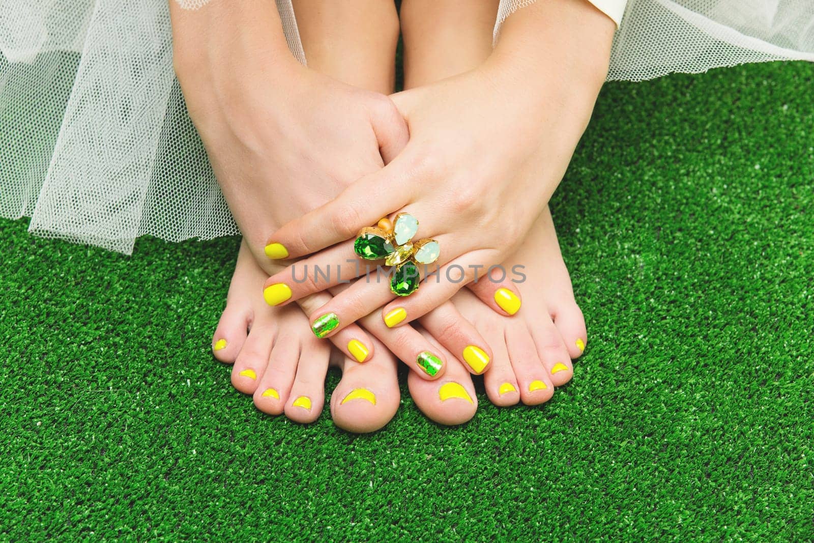 Closeup of woman toes and fingers with yellow, green nail polish.