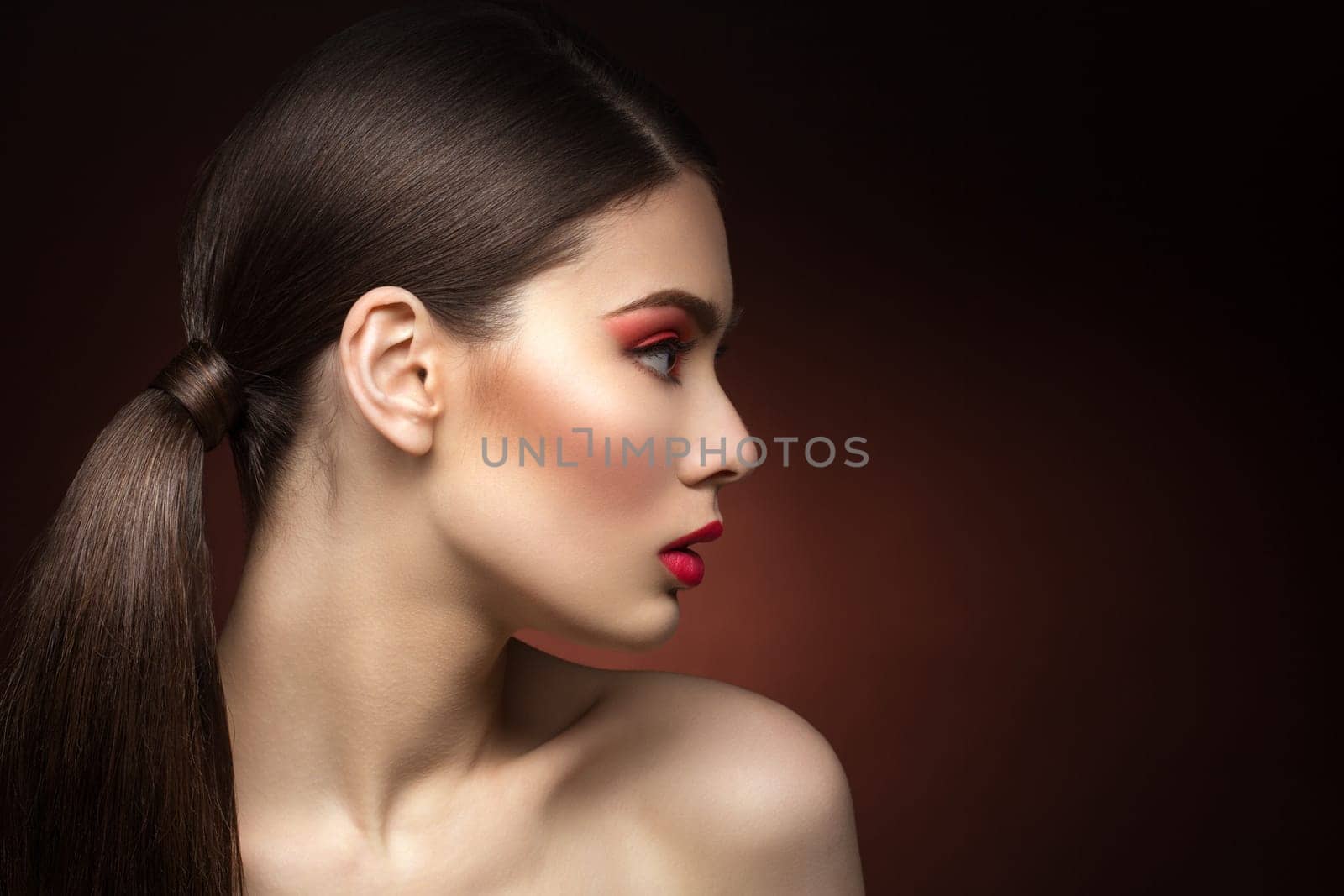 Closeup of young woman profile with red lips. Over dark background. Copy space.