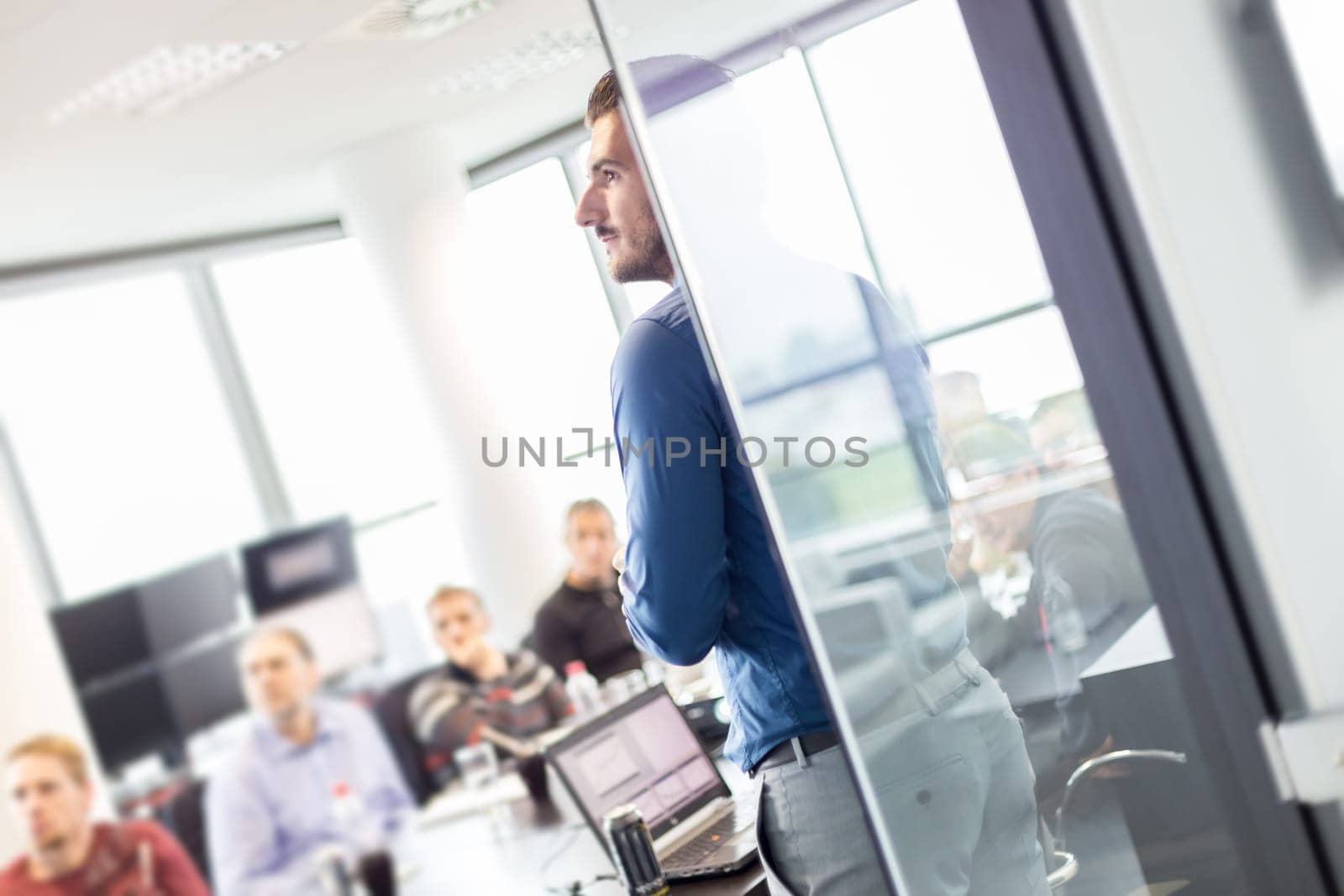 Business man making a presentation at office. Business executive delivering a presentation to his colleagues during meeting or business training. View through glass. Business and entrepreneurship.
