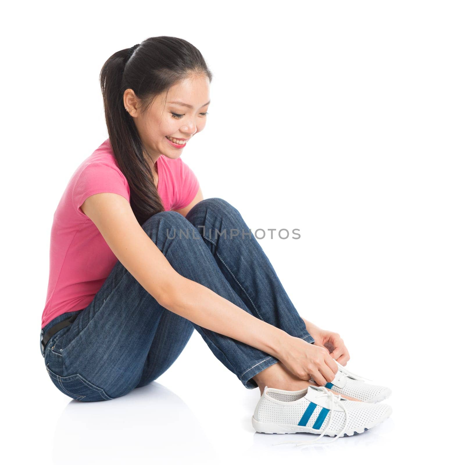 Portrait of young Asian woman in pink shirt and jeans wearing shoes, full body seated isolated on white background.