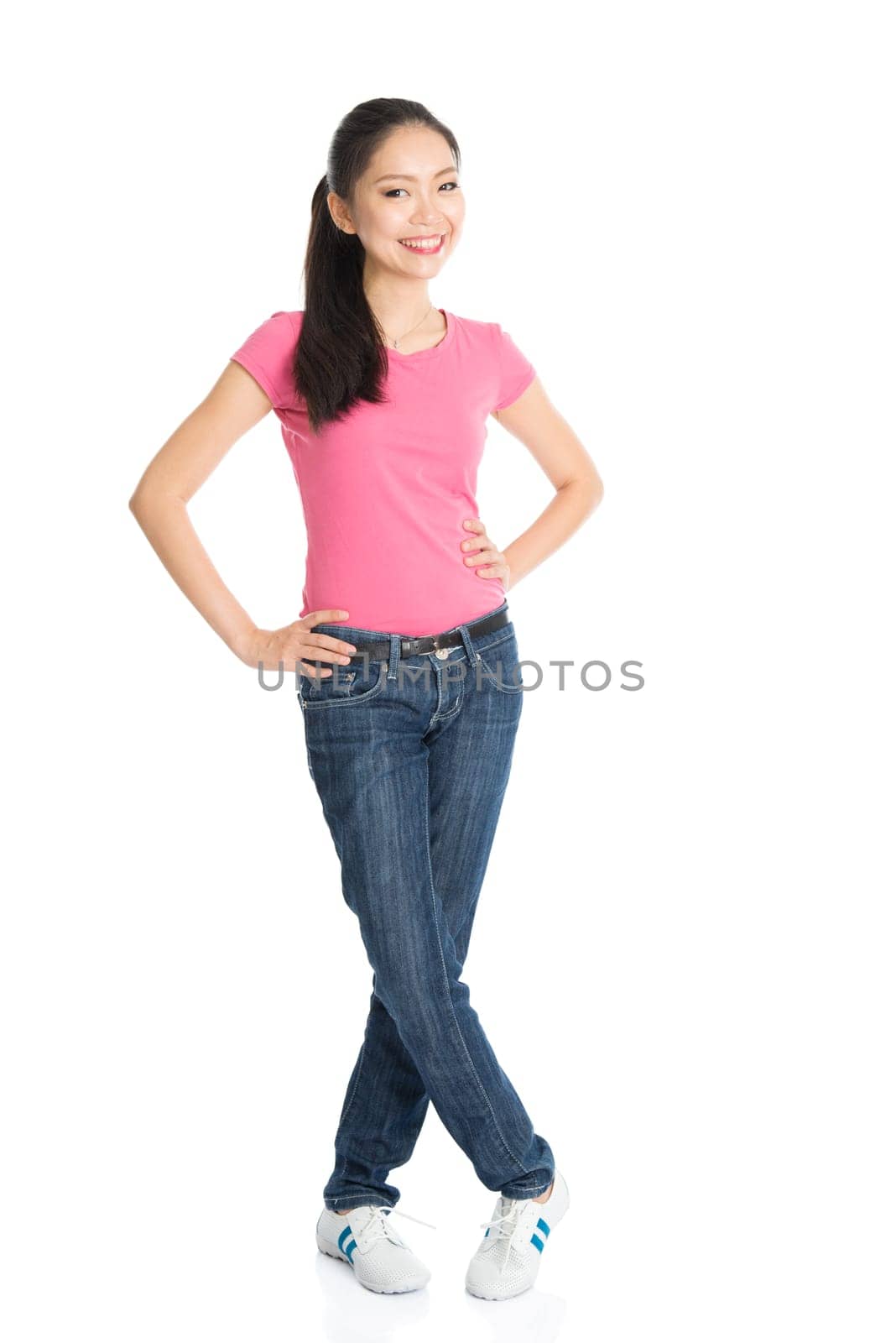 Portrait of young Asian female in pink shirt and jeans with ponytail hair is smiling, full length standing isolated on white background.