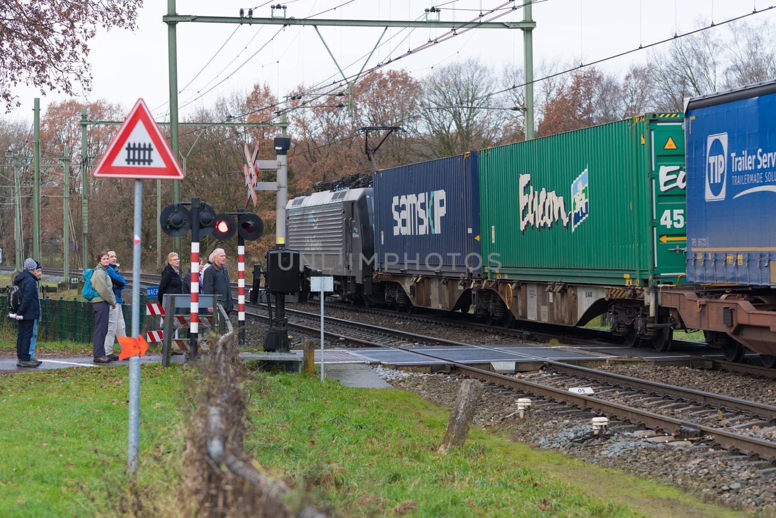 OLDENZAAL, NETHERLANDS - NOVEMBER 27, 2016: Unknown people waiting for a passing container train on a secured train crossing