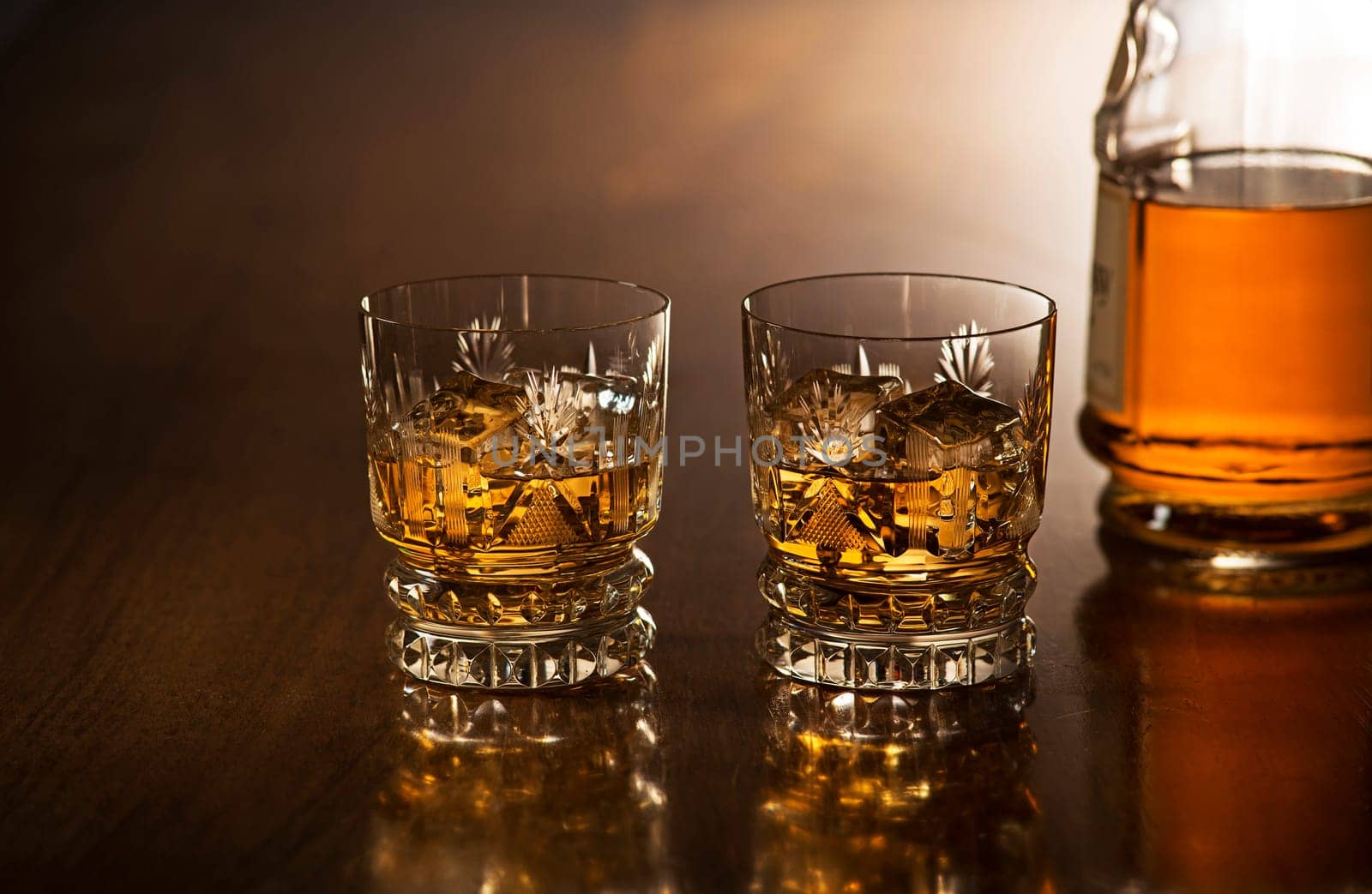 Whiskey with ice in glasses, rustic wood background.