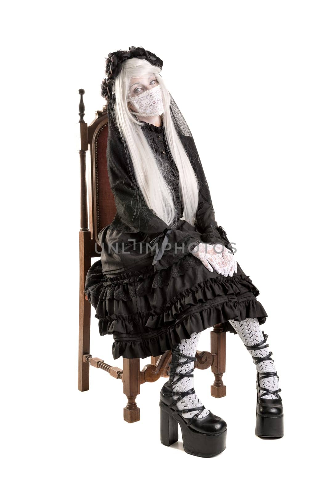 Girl in a black dress with white eyes looking like a doll in a chair isolated in white