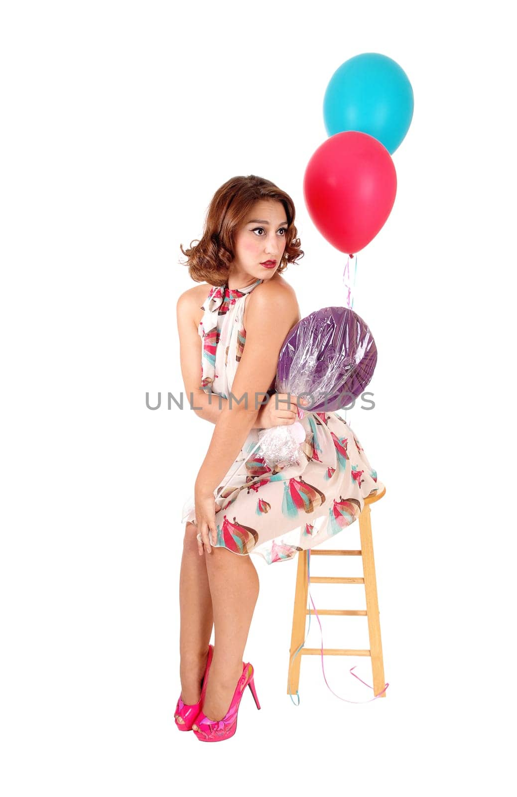 A beautiful young woman siting on a chair, holding.a lollypop and balloons, isolated for white background..