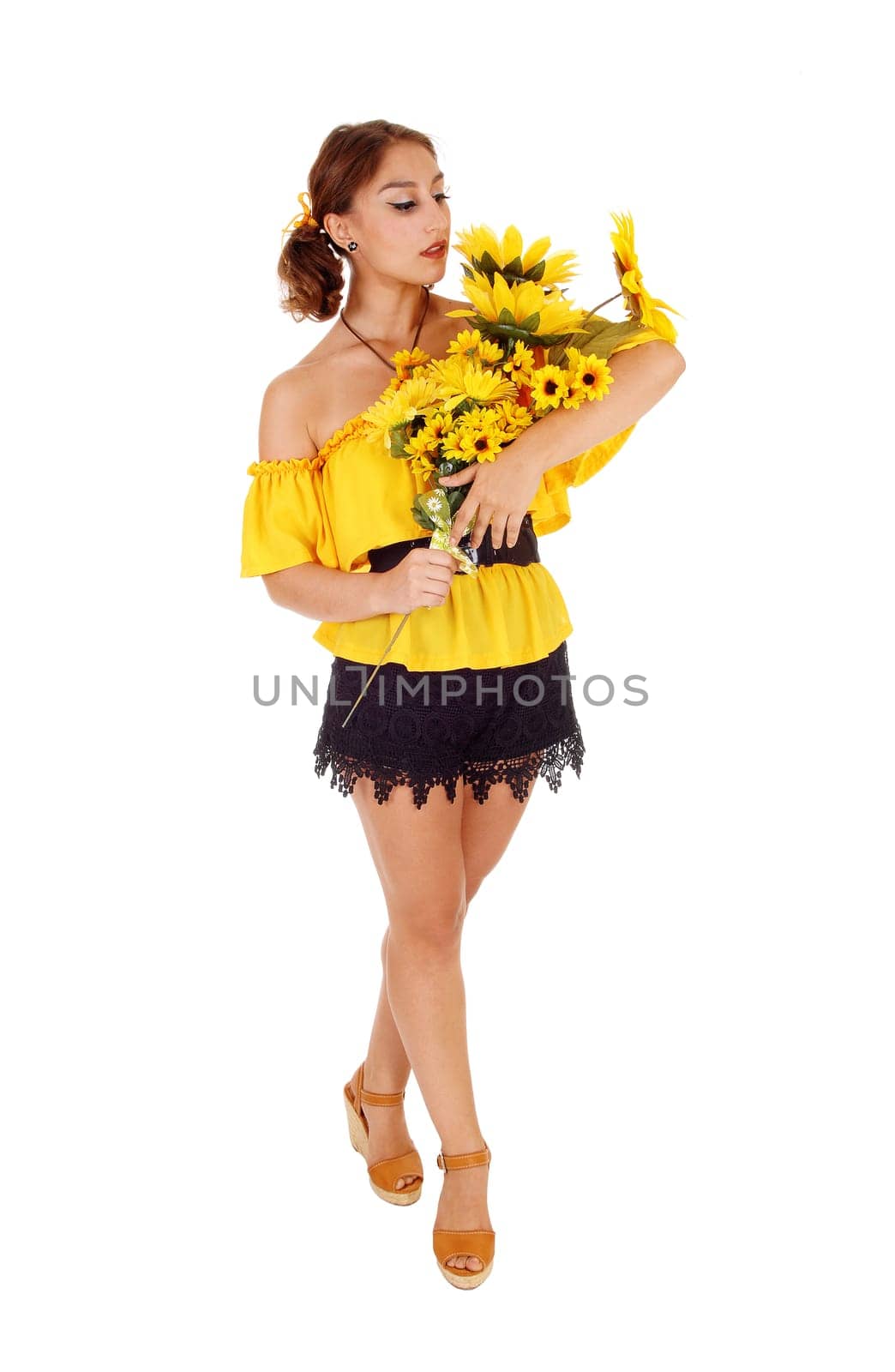 Gorgeous young woman in a yellow blouse holding a bunch of .sunflowers, looking at them, standing isolated for white background..