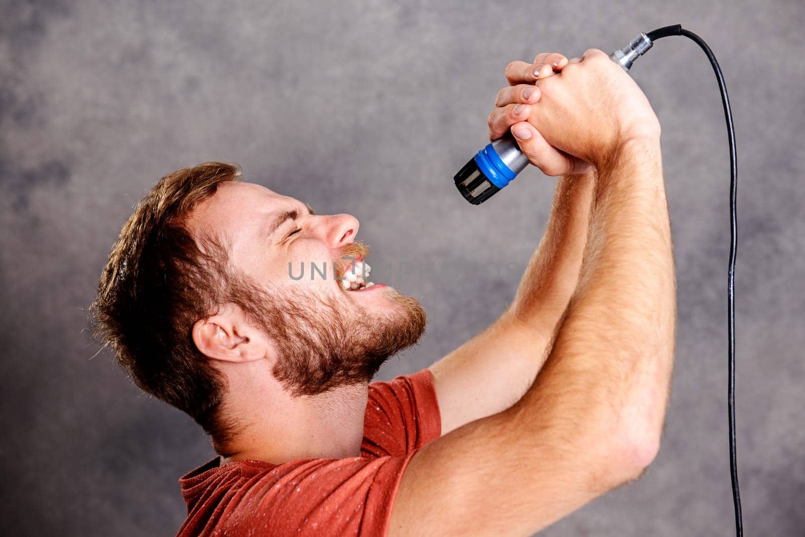 young bearded man in red shirt singing in microphone