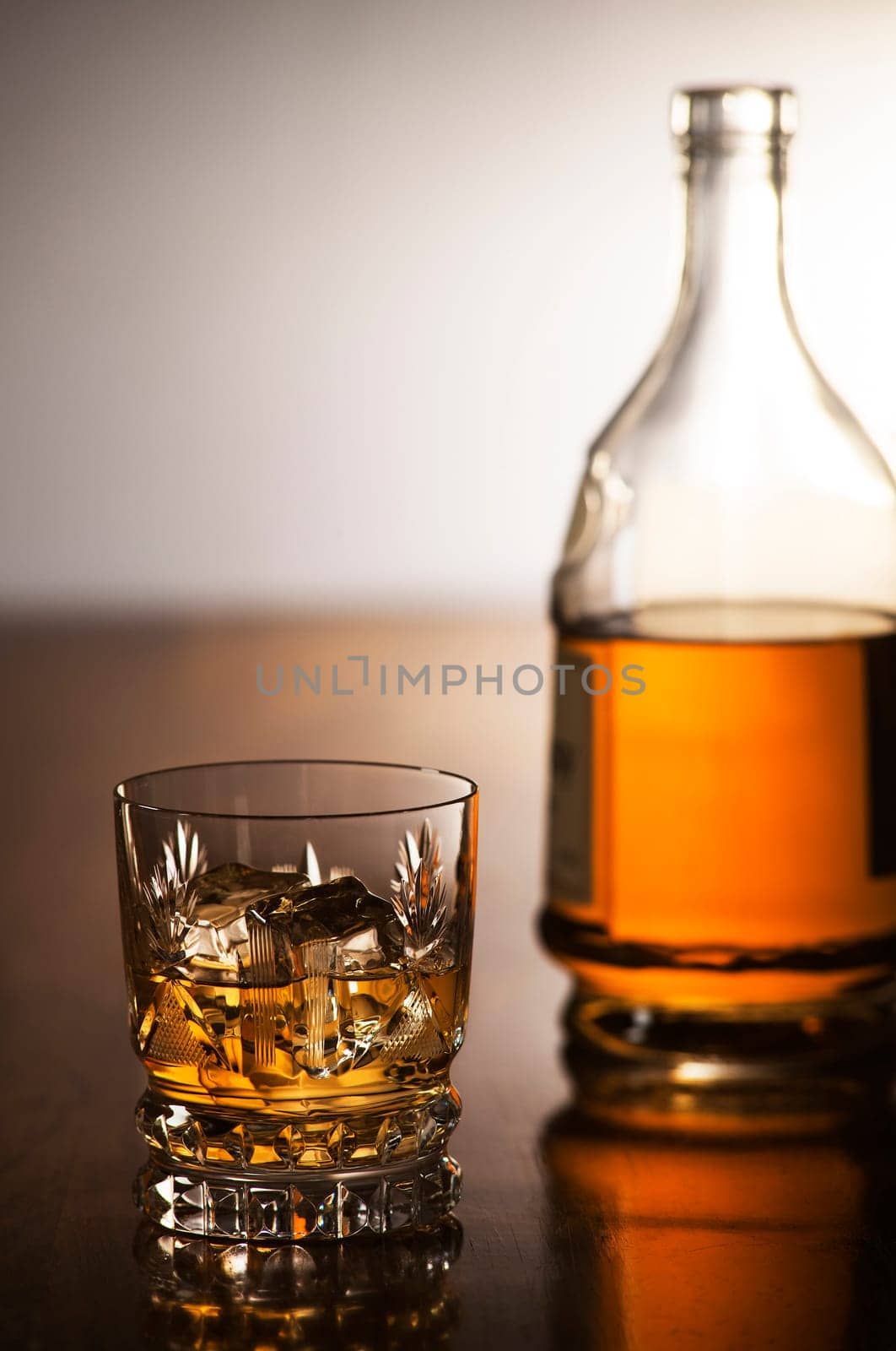 Whiskey with ice in glass and bottle on wooden background