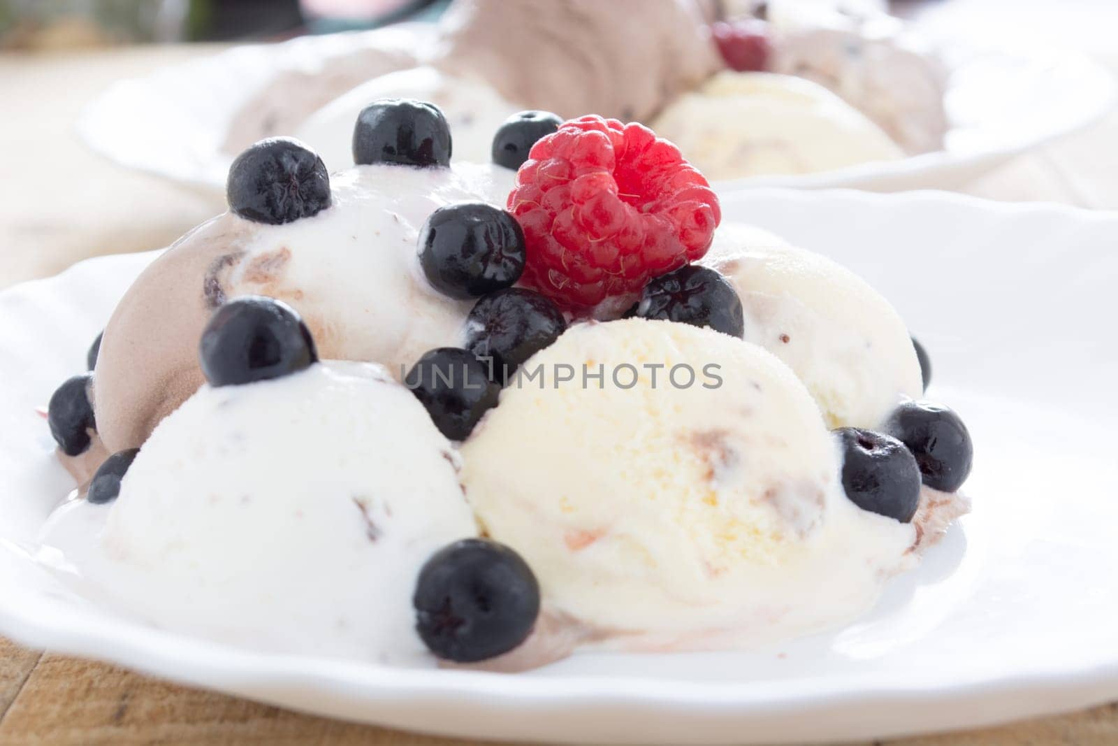 Scoops of chocolate ice cream in the white plate with raspberries and chokeberries