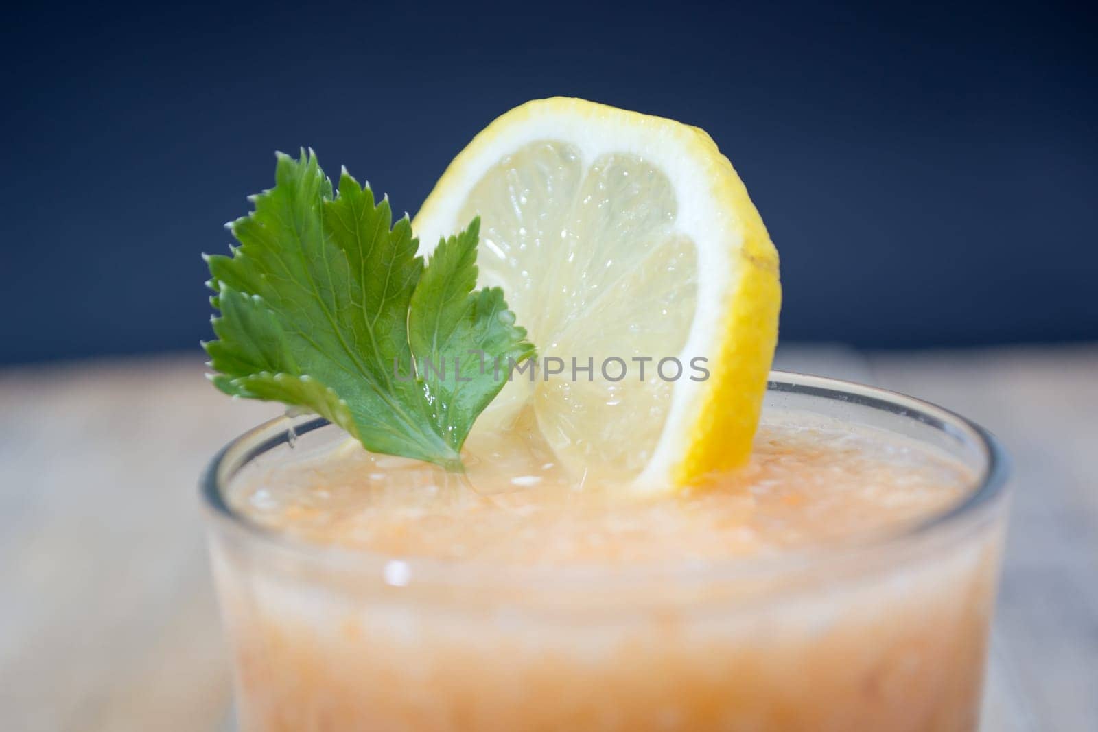 Fresh lemonade with ginger decorated with green celery leaves and lemon on the dark background