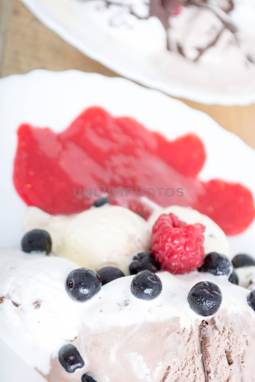 Scoops of chocolate ice cream in the white plate with raspberries and chokeberries