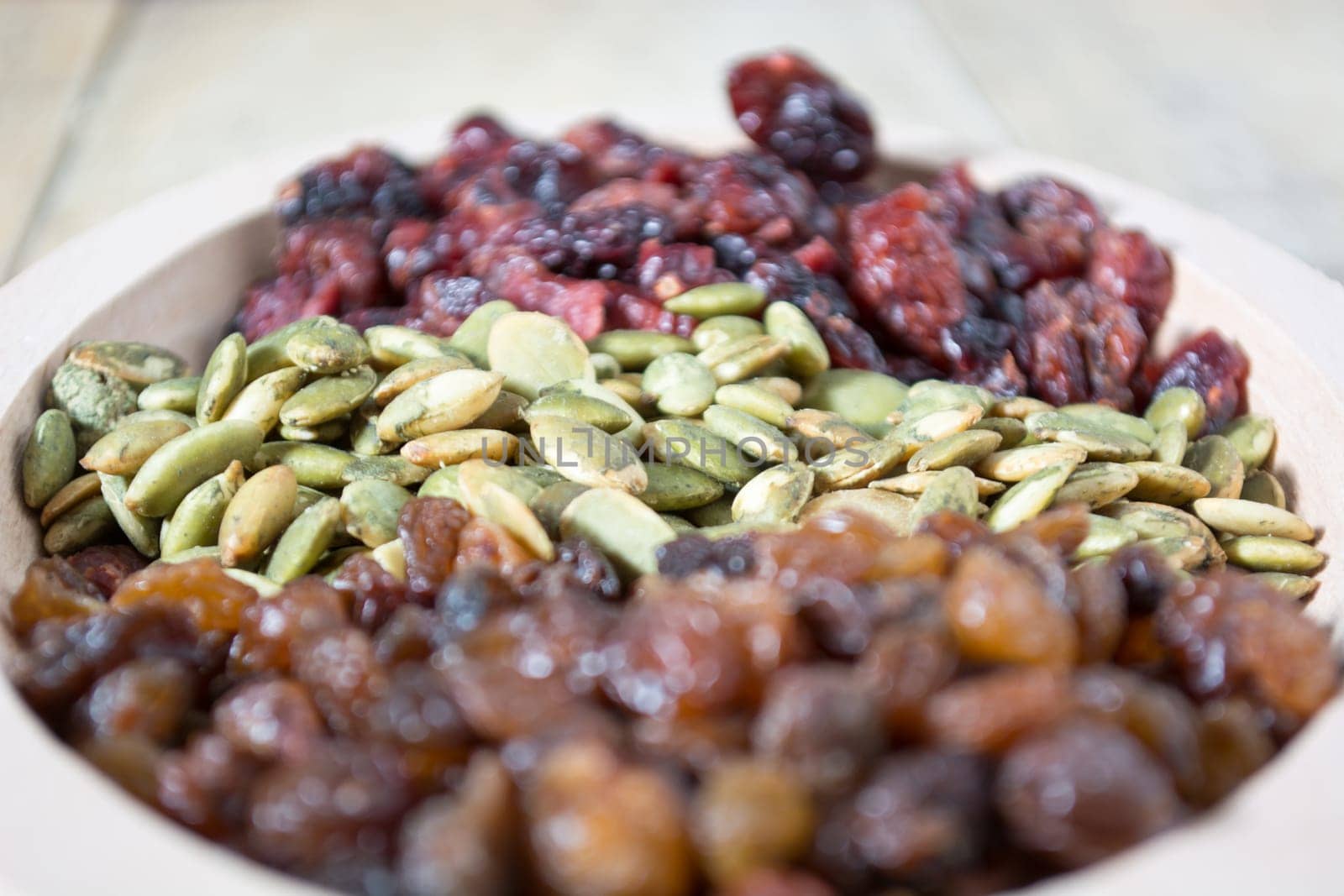 Bowl full with dry fruits and pumpkin seeds on the wooden table, shoot with selective focus