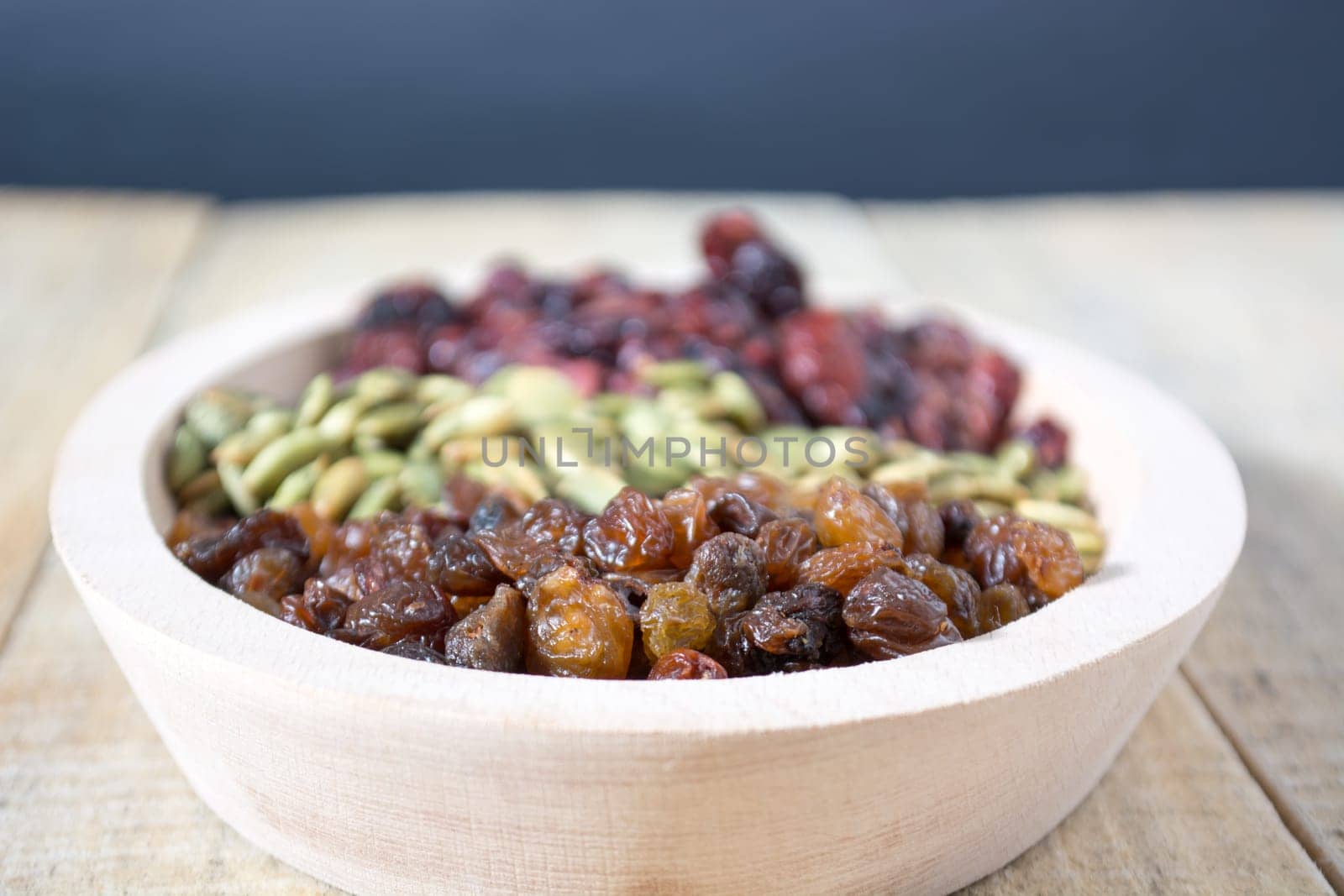 Bowl full with dry fruits and pumpkin seeds on the wooden table, shoot with selective focus