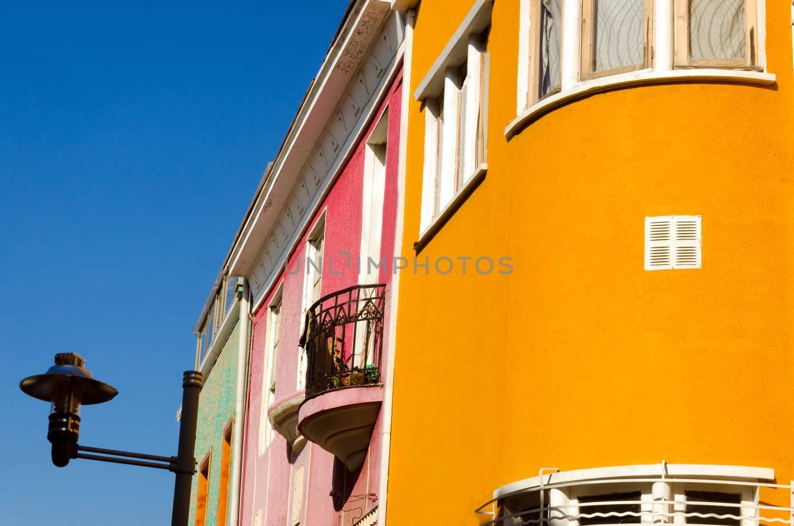 A curve of orange joins with a small balcony on a pink wall, and completes the journey with a street lamp in Valparaiso, Chile
