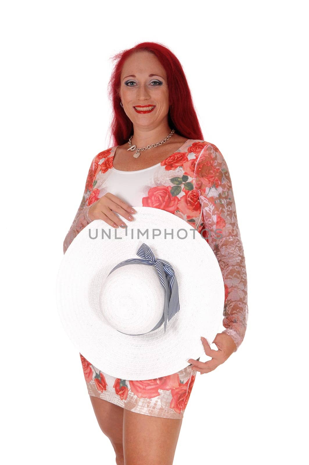A beautiful woman in a summer dress, holding a white.hat in front of her, in a portrait image, isolated for white background..