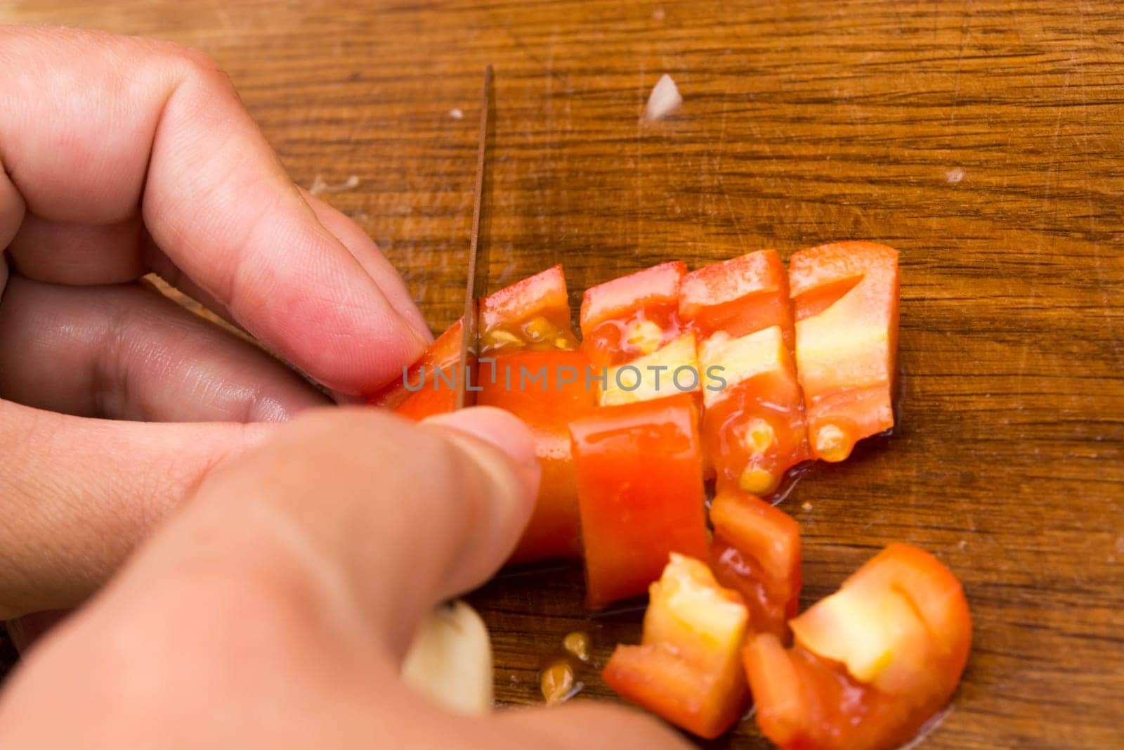 Cutting and chopping  tomato on a wooden plate. Preparing it for a salad