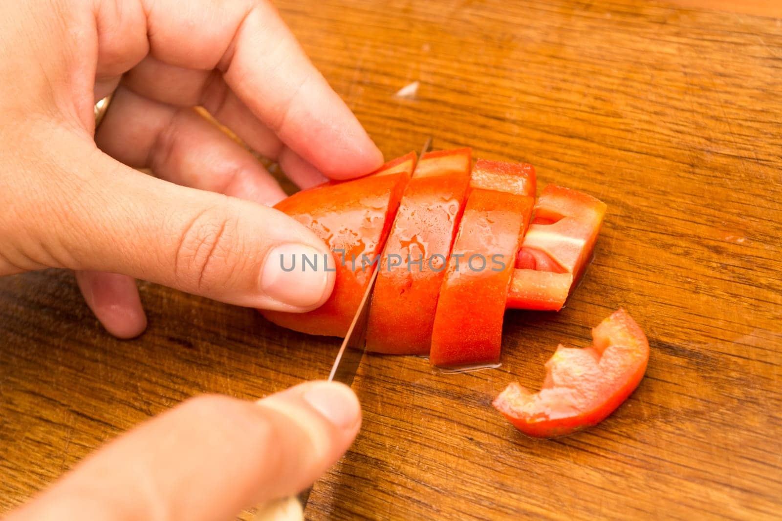 Cutting and chopping  tomato on a wooden plate. Preparing it for a salad