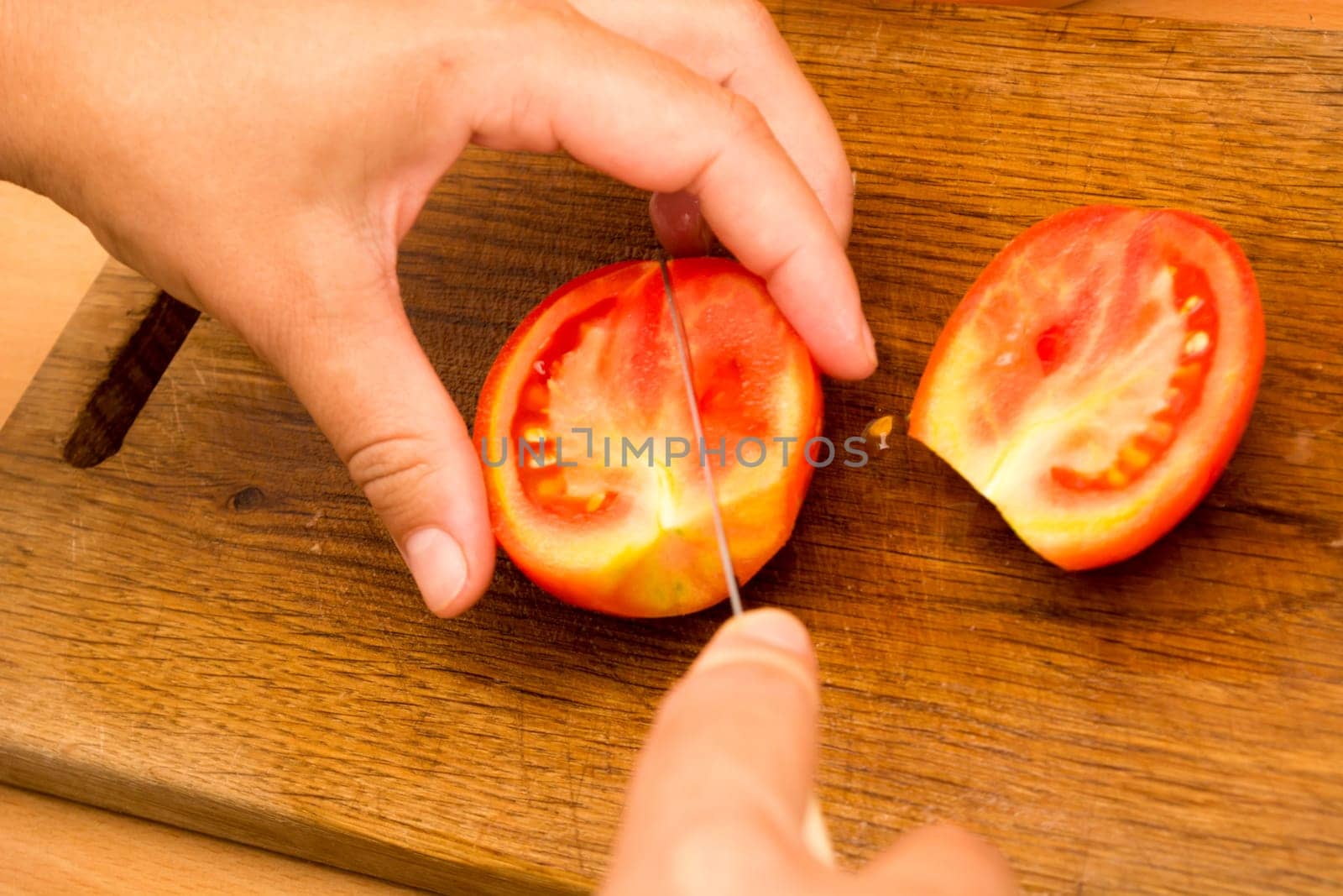 Cutting and chopping  tomato on a wooden plate. Preparing it for a salad