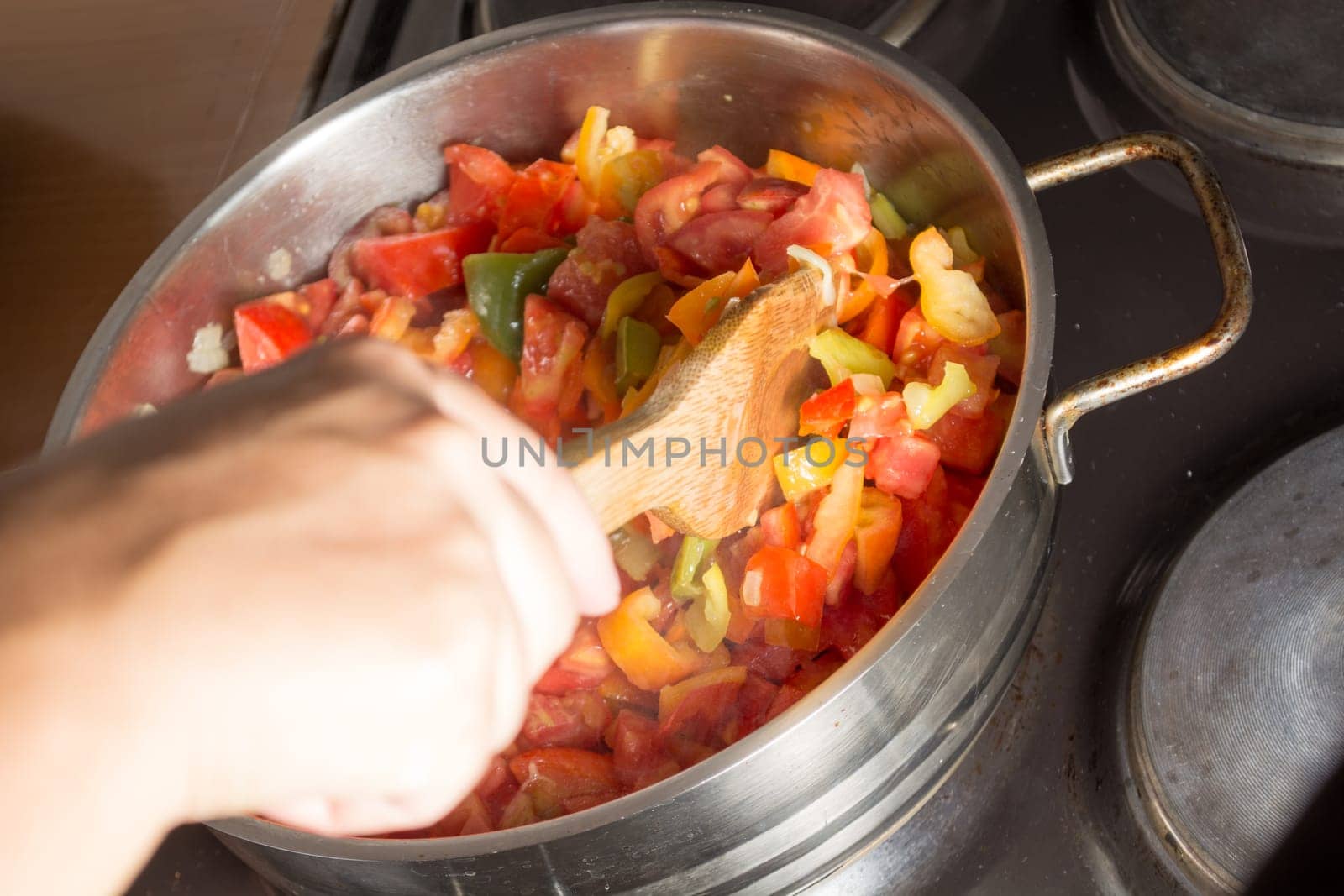 Cooking stew with fresh vegetables in a pot. Mixing it with mixing spoon