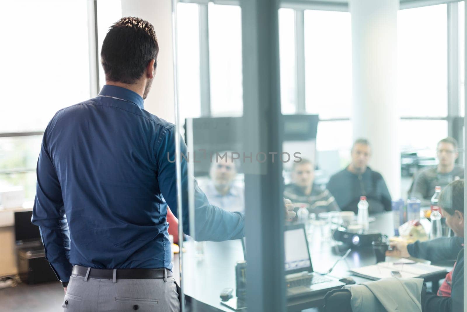 Business man making a presentation at office. Business executive delivering a presentation to his colleagues during meeting or in-house business training. Rear view. Business and entrepreneurship.