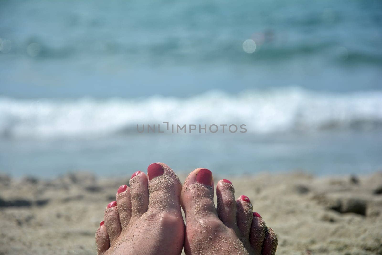 Sandy feet with red toenails on the beach with blurred sea in the background