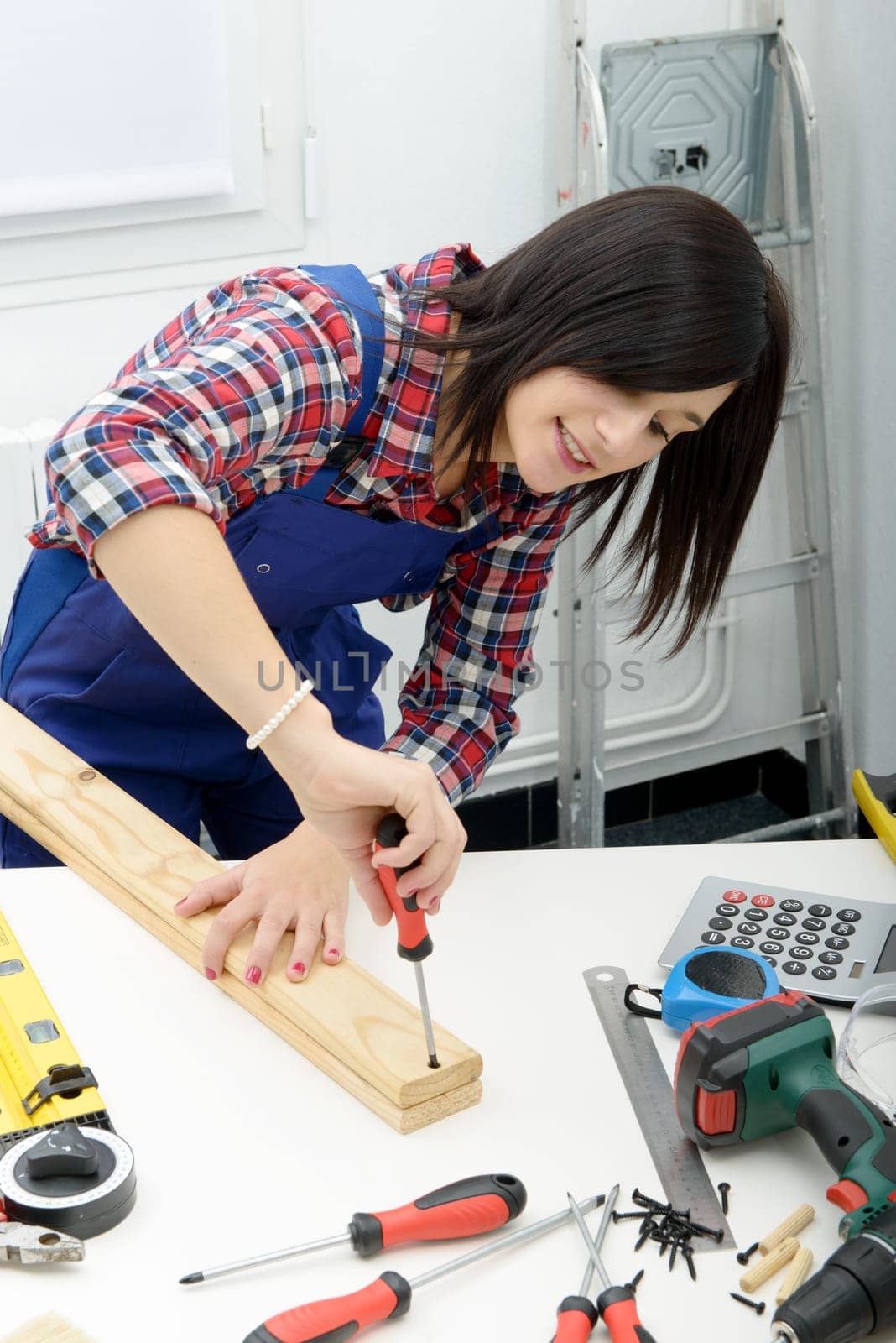 smiling young woman assembling wooden planks using screwdriver