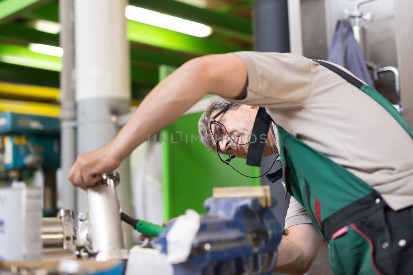 Industrial worker with protective mask welding inox elements in steel structures manufacture workshop or metal factory.