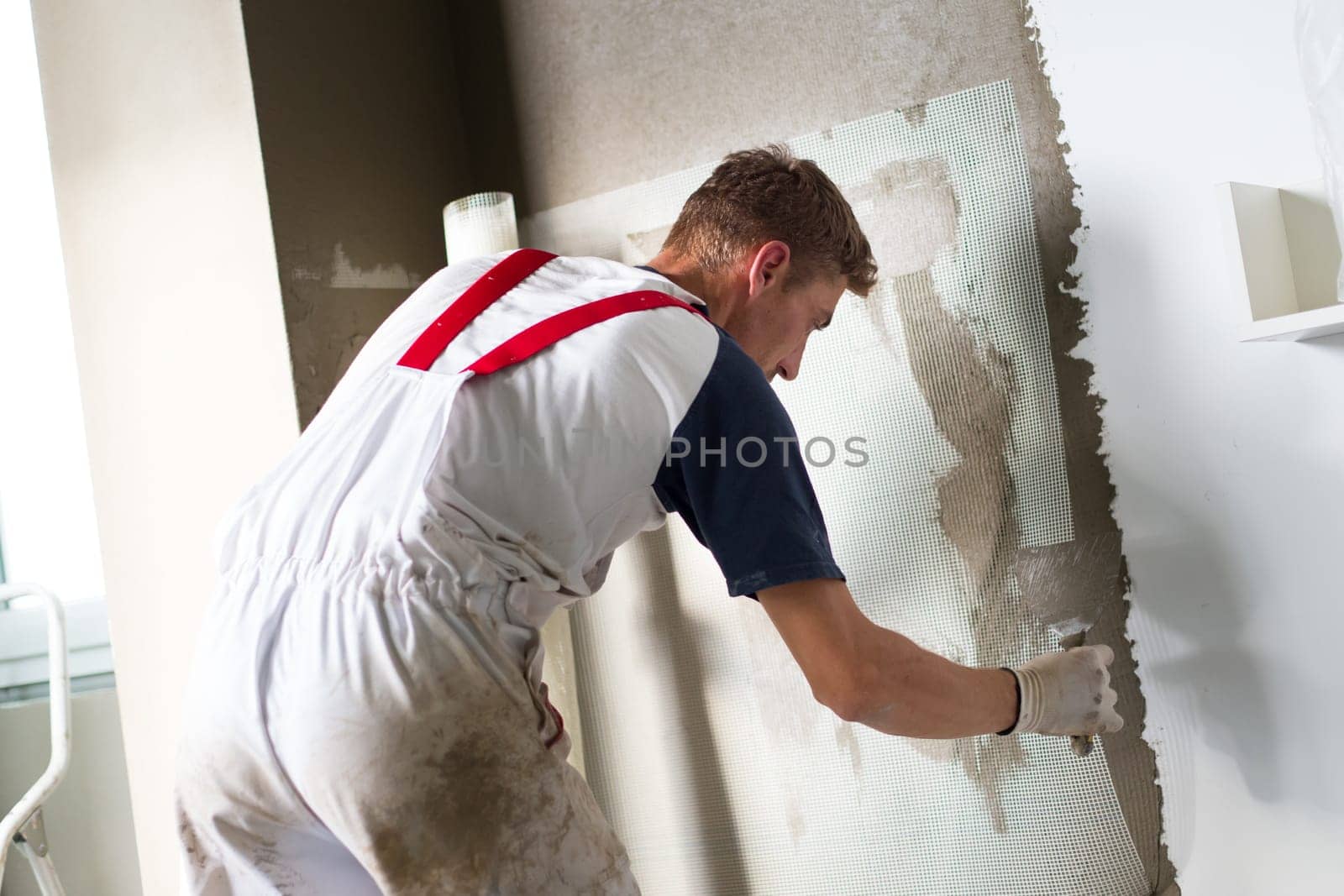 Thirty years old manual worker with wall plastering tools renovating house. Plasterer renovating indoor walls and ceilings with float and plaster.