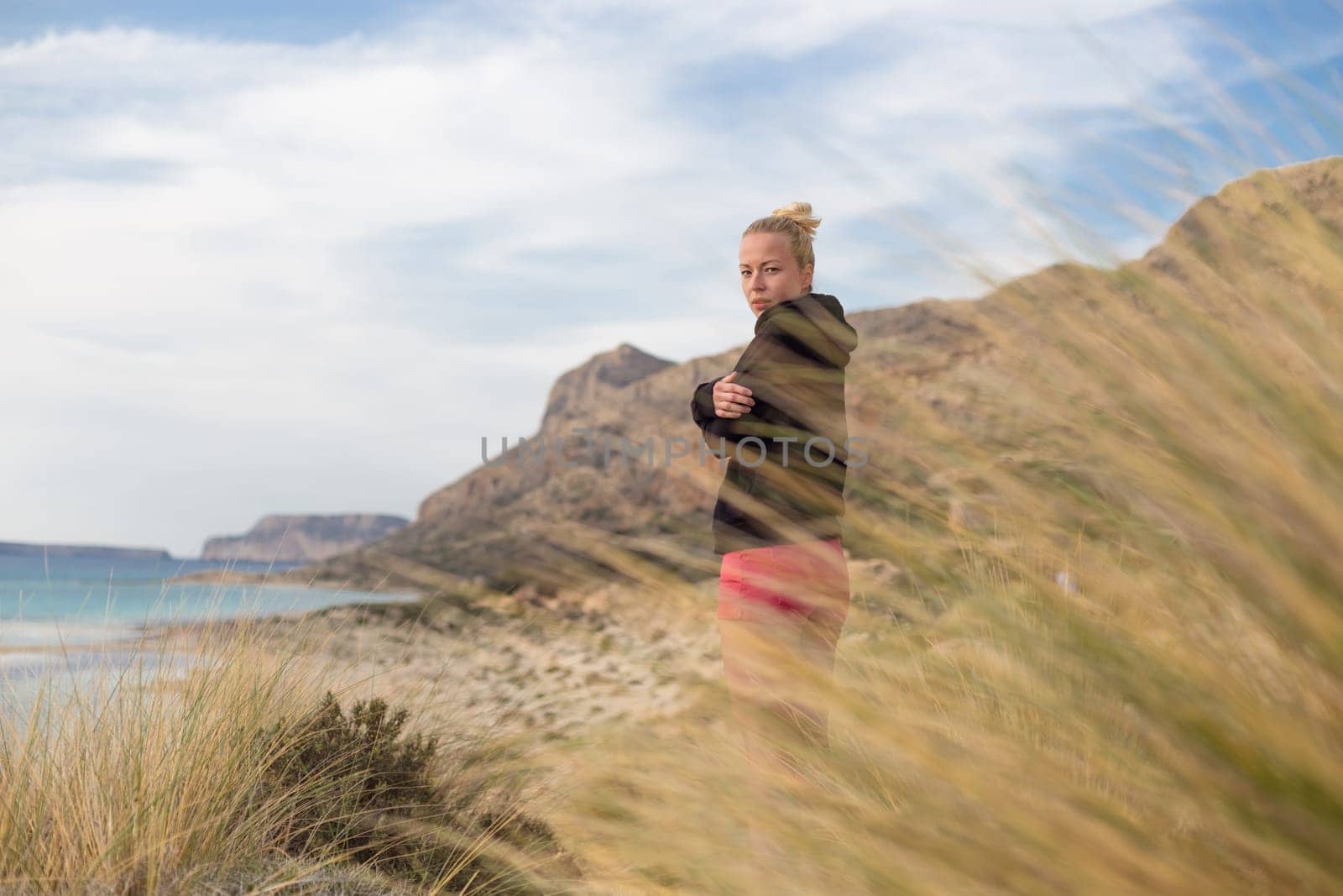 Woman, arms crossed, feeling chilled, enjoying last autumn sun, an beautiful Balos beach. Concept of vacations, freedom, happiness, enjoyment and well being.