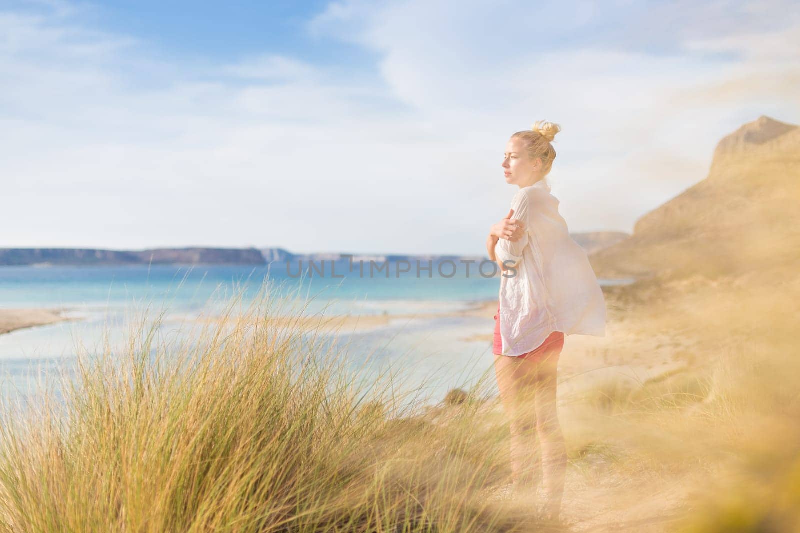 Woman, arms crossed, feeling chilled, enjoying last autumn sun, an beautiful Balos beach. Concept of vacations, freedom, happiness, enjoyment and well being.