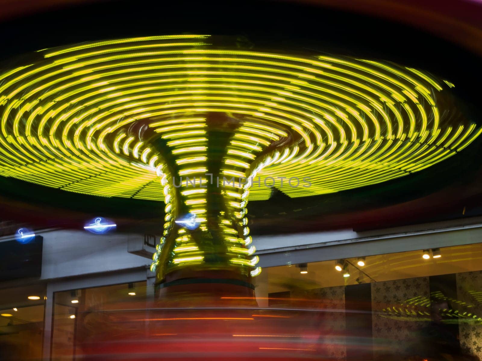 Flat-angled view of a kids funfair in motion at night with yellow stripes of light on a Christmas market.
