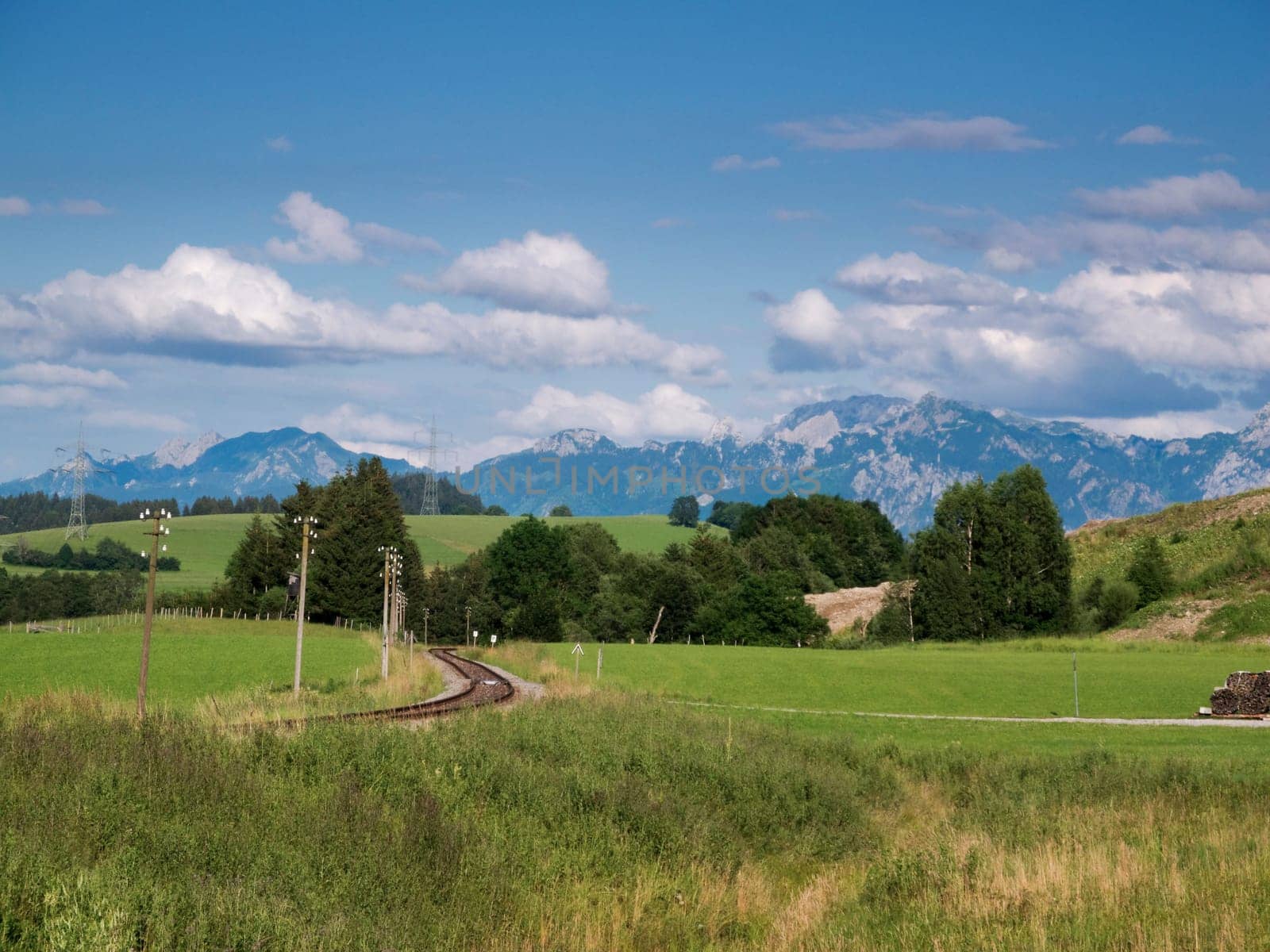 Landscape view in the Allgäu (Bavaria) with railway track,green meadow and blue sky with white clouds in summer.