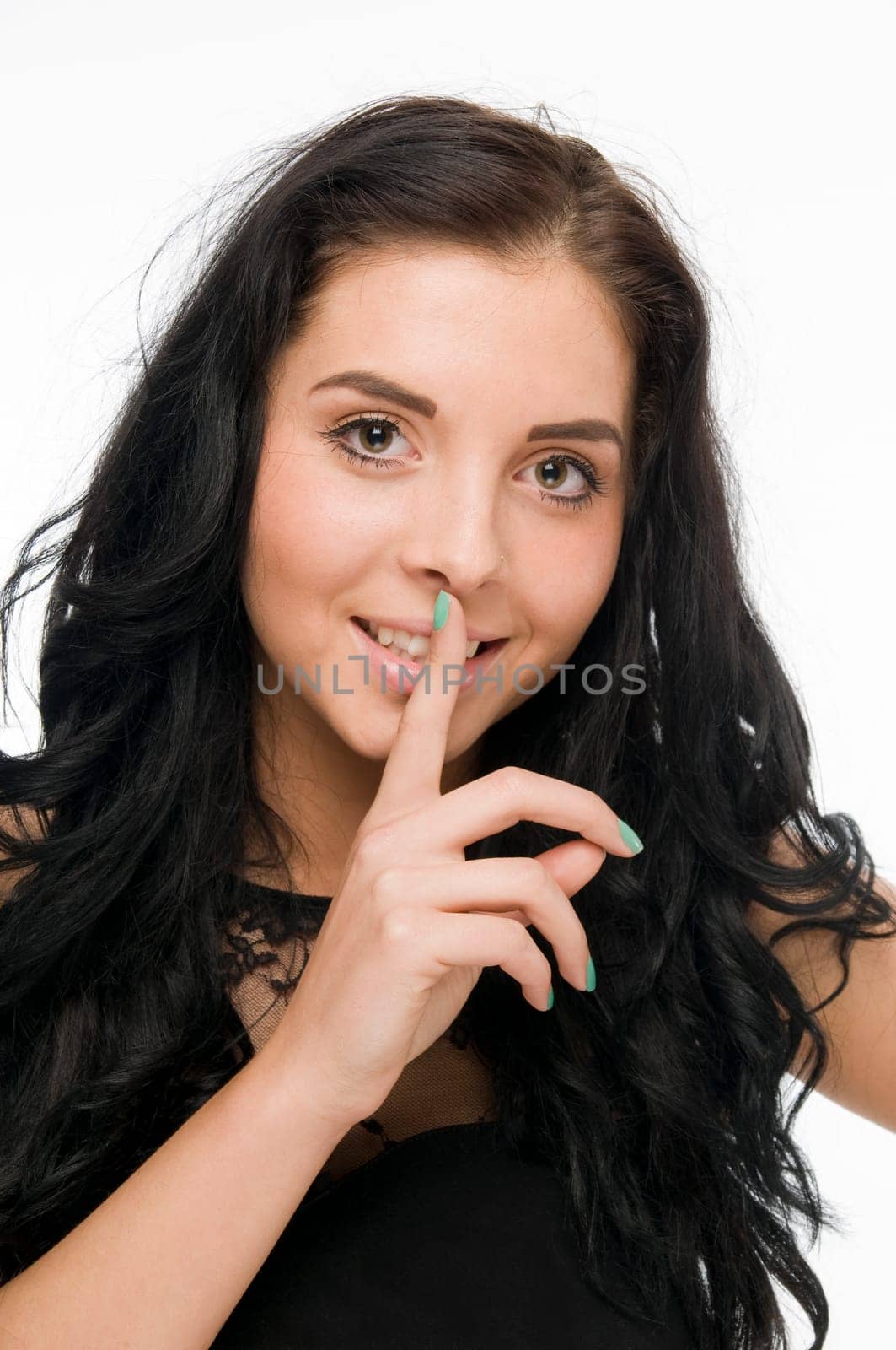 Frontal head-and-shoulders view of a young black-haired woman against a white background holding her index finger in front of her mouth and smiling into the camera.