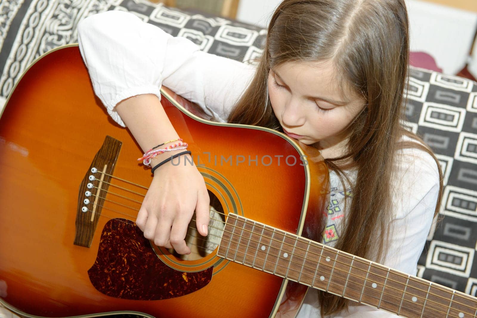 Young teen girl playing acoustic guitar on sofa