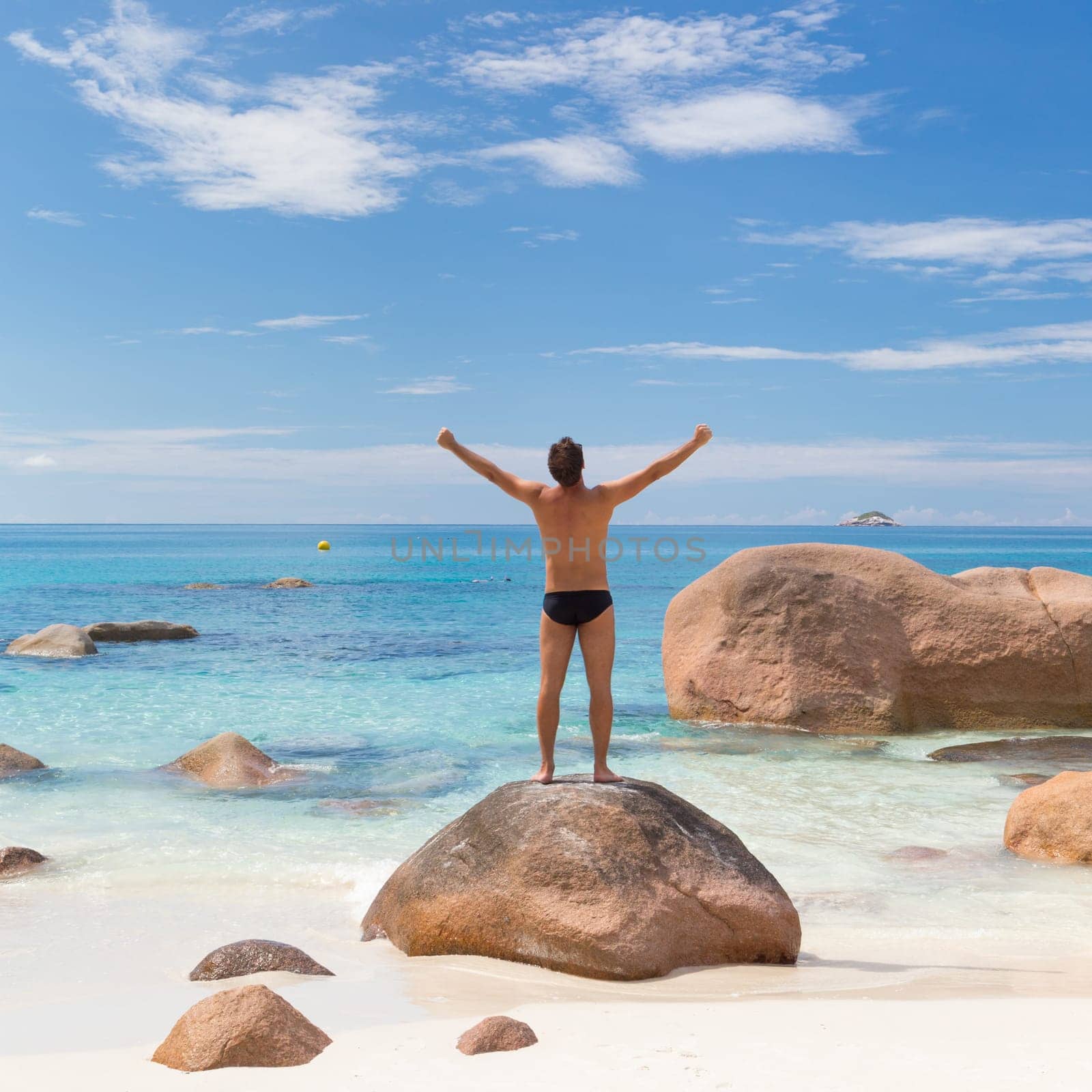 Successful man wearing black swimwear, enjoying amazing view on Anse Lazio beach on Praslin Island, Seychelles. Summer vacations on picture perfect tropical beach concept. Copy space.