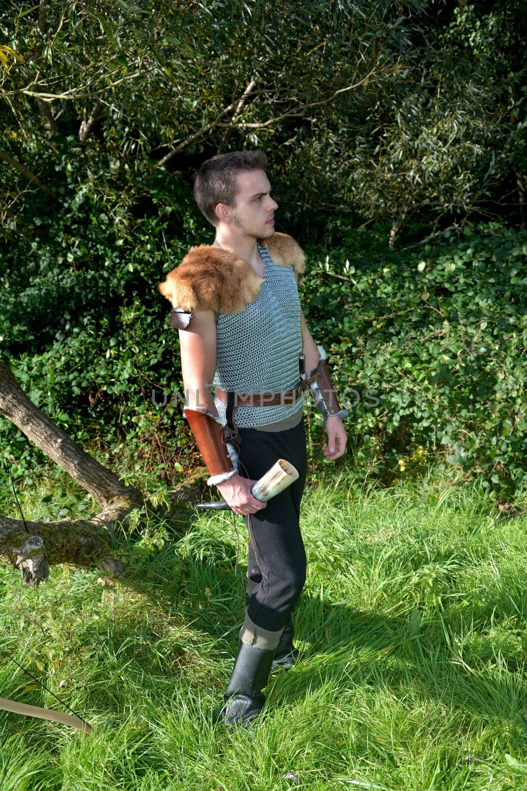 Medieval-dressed man stands in nature,holds drinking horn in his hand and looks to the right