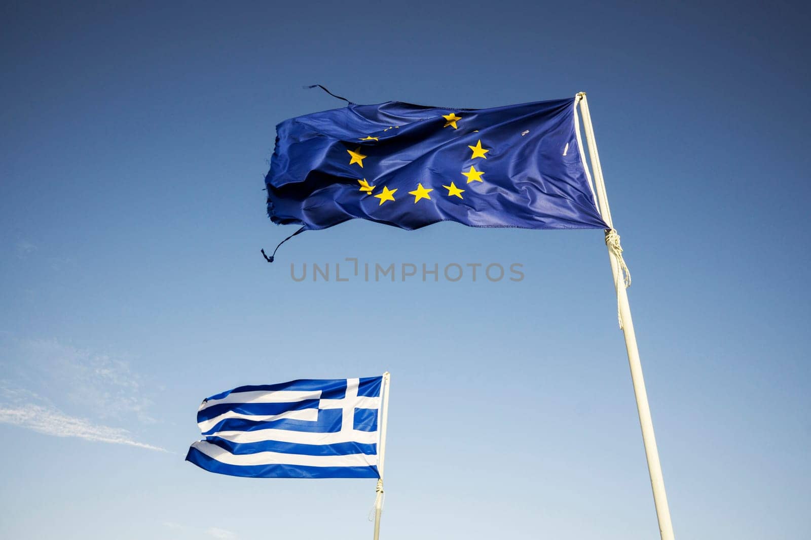 Ripped european Union flag and Greek flag, waving in the wind