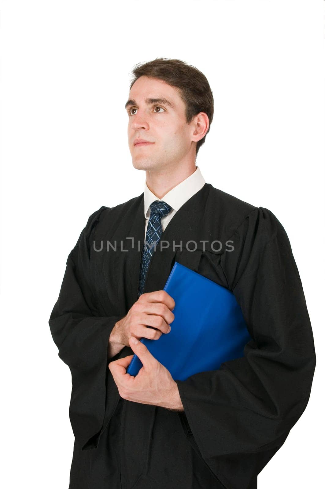 Side upper body view of a young man in black robe and blue writing folder under the arm against a white background looking sideways upwards.