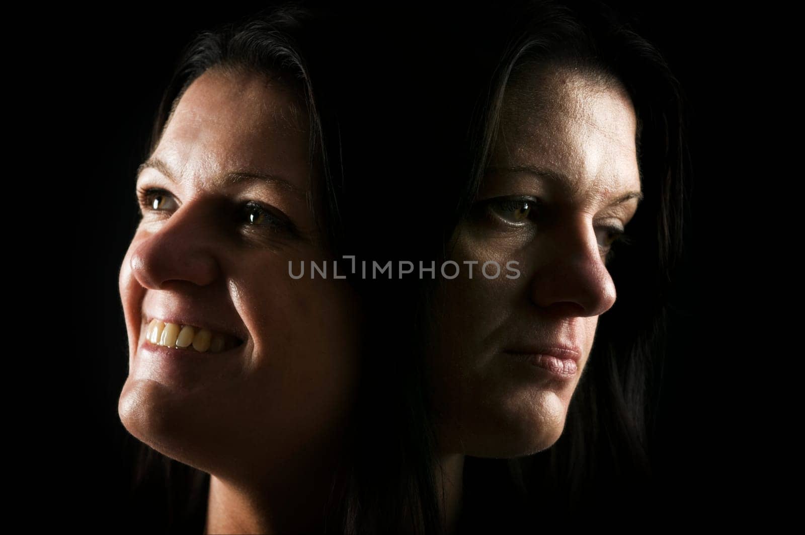 Double exposure head of a middle-aged woman with happy and sad facial expression against a black background.