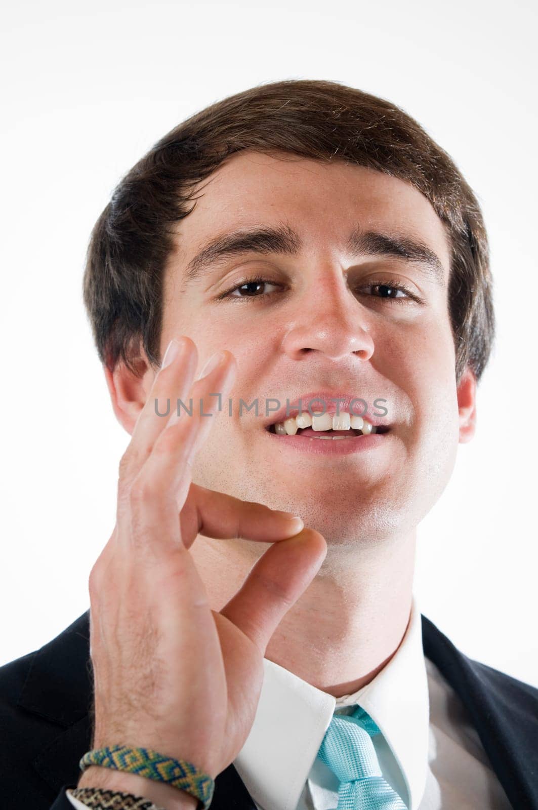 Head-and-shoulder view of a young man in business dress shows the O.K. sign with his right hand against a white background.