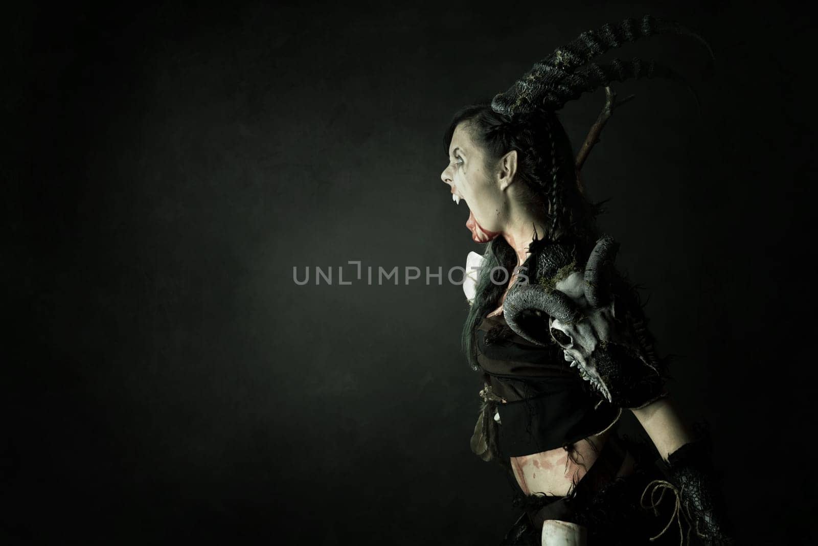 Faun sorceress with big horns and blood against a dark background