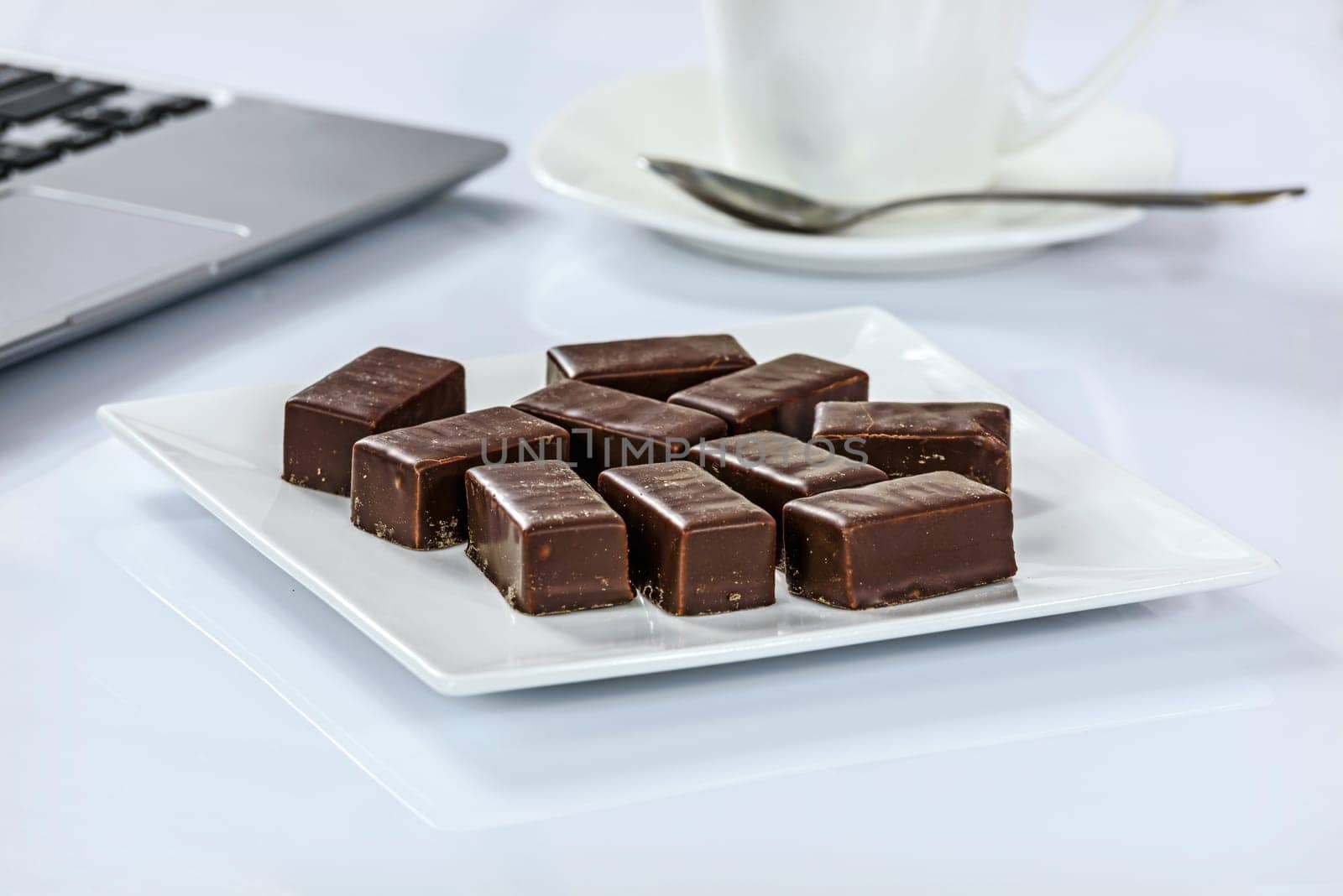 Chocolates on a plate next to a cup of coffee and laptop in the office