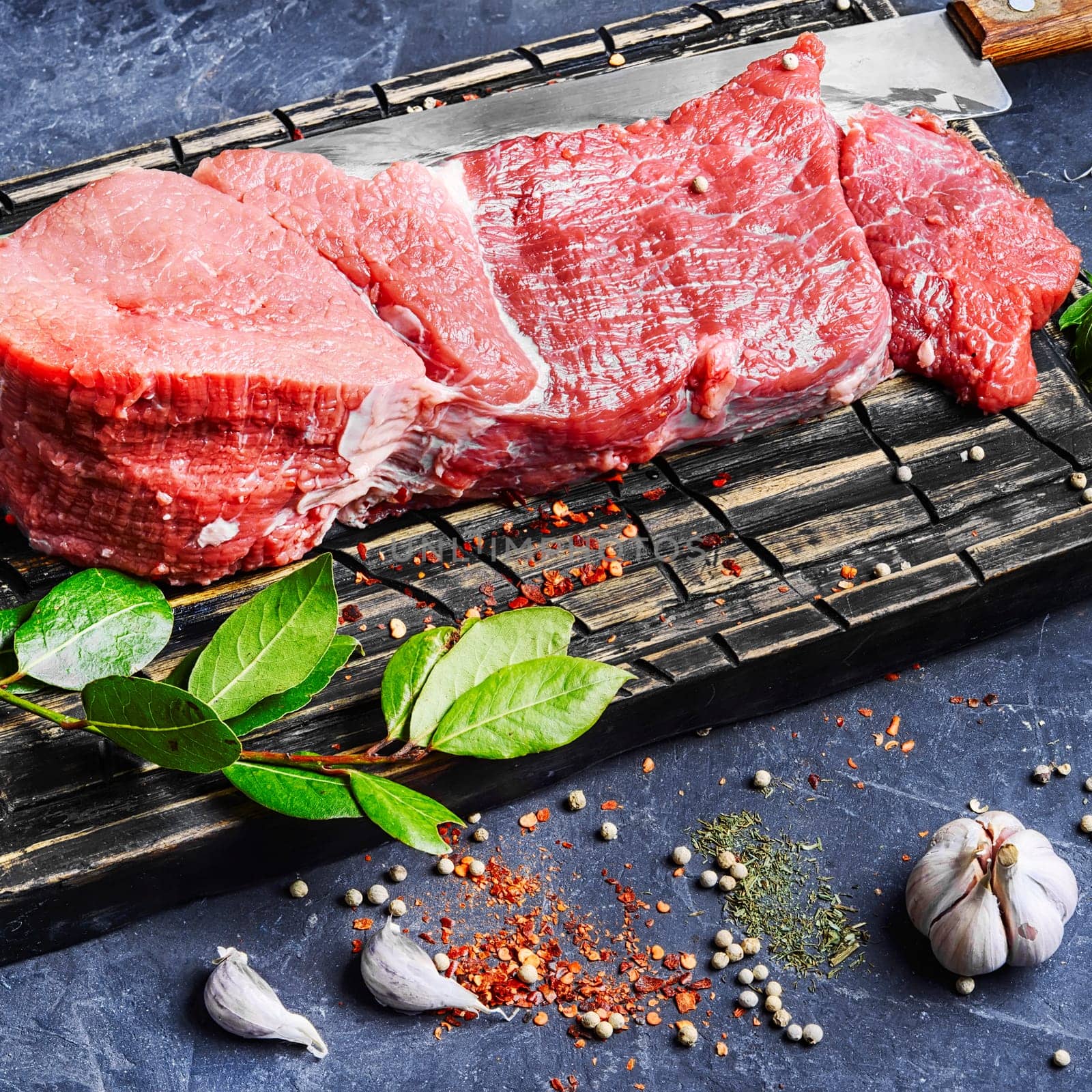 Raw beef steak and laurel branch on cutting board