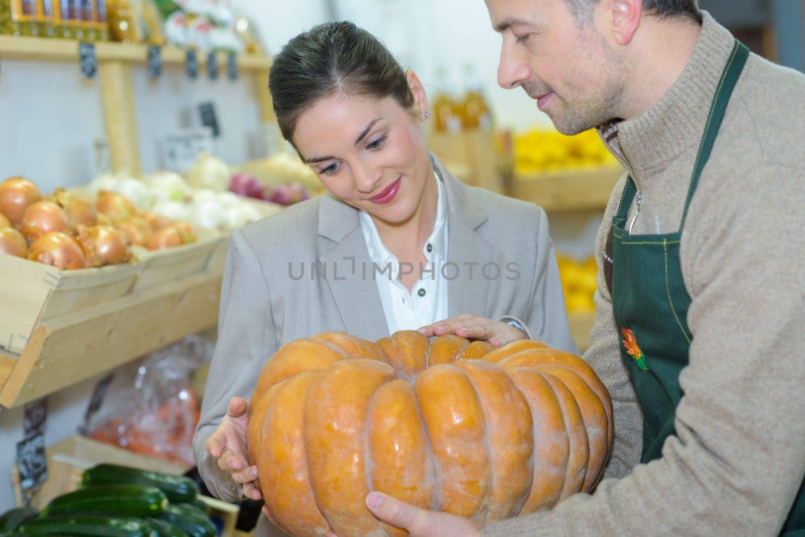 Grocer showing pumpkin to customer